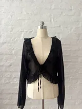 Blusa corta negra de mangas largas acampanadas, con volados en el escote y lazo ajustable en el frente.