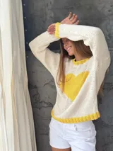 Sweater tejido a mano en Uruguay, 100% lana merino color crudo, con cuello, puños y ruedo en amarillo. Presenta un corazón amarillo en el frente.