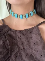 Gargantilla corta con cuentas de piedra color turquesa, ojos de tigre color marrón, resina color verde y cristales facetados color rosa. Se cierra con cadena de acero quirúrgico y ganchito para ajustar.