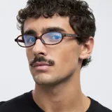 Montura de lentes para computadora con filtro de luz azul, de forma ovalada y montura gruesa con patrón carey (tortoise). Las patillas son de color blanco translúcido en la parte superior y carey en la parte inferior.