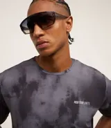 Remera deportiva negra con estampado manchado en gris y lettering en el pecho. Confeccionada en tejido dry de poliéster y elastano, con cuello redondo y mangas cortas.