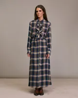 Vestido largo camisero con estampado a cuadros en tonos azul, marrón y beige. Presenta cuello camisero con volantes y mangas largas. Incluye cinturón de la misma tela para ajustar a la cintura.