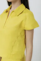 Blusa amarilla de lino con cuello polo, mangas cortas y cierre frontal con cremallera.