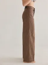 Pantalón gris de tiro medio alto, corte ancho, con bolsillos delanteros y traseros, detalles de atraques y triples costuras en color amarillo.