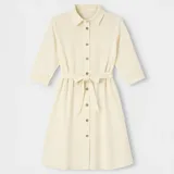 Vestido camisero color crema con botones frontales, cuello camisero y mangas 3/4. Incluye cinturón de la misma tela para ajustar a la cintura.