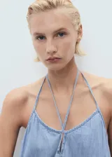 Vestido largo de mezclilla, color azul claro, con escote de pico y tirantes finos ajustables. Presenta un detalle de lazo en el centro del escote y un corte recto que se ensancha ligeramente hacia el ruedo.