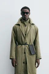 Trench color verde oliva de tejido técnico, corte relaxed fit, cuello solapa, manga larga, bolsillos laterales y abertura en la espalda.