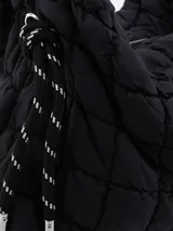 Bandolera negra acolchada con diseño geométrico de rombos, cierre superior con cremallera y correa de cuerda gruesa ajustable.