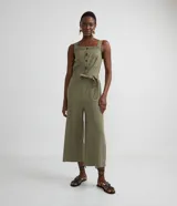 Mono pantacourt verde militar de viscosa y poliéster, con escote cuadrado, tirantes anchos con pespuntes, botones frontales contrastantes, cinturón con pespuntes para amarrar y bolsillos laterales.