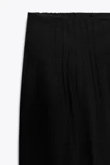 Pantalón negro con bordados florales en los laterales, tiro alto, cintura elástica en la parte trasera, bolsillos laterales, pliegues y cierre frontal con cremallera, botón interior y gancho metálico.