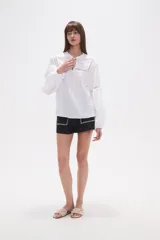 Blusa holgada de algodón color rosa pálido, con escote redondo y lazo ajustable en el centro. Presenta detalles de encaje calado alrededor del escote y en los puños de las mangas largas abullonadas.