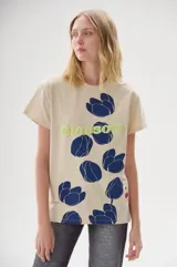 Remera color crema con estampado de flores azules y texto "Blossom" en verde.