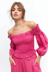 Crop top blanco con escote off-shoulder, punto panal en el torso y volados en el escote.