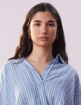 Blusa celeste y blanca a rayas verticales, con cuello con solapa y escote en V. Delantera cruzada con abertura simulada y mangas cortas.