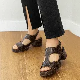 Sandalias de cuero vacuno color marrón con textura tipo cocodrilo, taco ancho y plataforma. Diseño con puntera descubierta y tira ancha sobre el empeine con aberturas laterales. Cierre con hebilla en el tobillo.