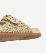 Sandalias planas doradas con puntera redonda, correas anchas con hebillas laterales y textura tejida.