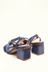 Sandalia de terciopelo verde con taco cuadrado de 7 cm, punta cuadrada y tiras anchas anudadas en el empeine. Cuenta con una tira fina ajustable al tobillo con hebilla dorada.