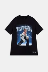 Buzo negro de manga corta con cuello redondo, parte de la colección Tini x Under Armour. Presenta un estampado frontal grande con un fondo azul eléctrico y destellos, mostrando a una mujer con chaqueta gris claro y pantalones oscuros, con la palabra "FUTTTURA" en tipografía brillante en la parte superior.