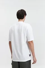 Remera beige de manga corta con textura y corte oversize. Presenta un pequeño bordado en relieve en el pecho.