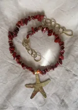 Collar corto con cuentas de piedra color ladrillo y detalles dorados. Dije grande de estrella de mar dorada con textura irregular.