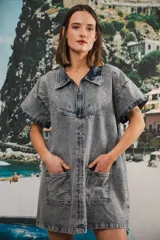 Vestido corto de denim celeste con efecto lavado, cuello camisero, cierre frontal con cremallera metálica, bolsillos delanteros y bordados de soles y símbolos en el canesú.