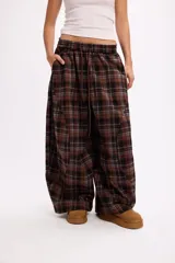 Pantalon de corte oversize y tiro medio, confeccionado en tela con estampado de cuadros en tonos marrones y negros. Presenta una silueta amplia y holgada con cintura elástica y cordón ajustable.