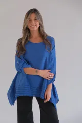 Blusa azul de lino con mangas 3/4 con botón para sujetar y ruedo irregular con detalle de rayas horizontales.