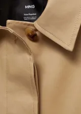 Abrigo largo color beige, con cuello camisero, cierre frontal con botones ocultos, lazo ajustable en la cintura, bolsillos laterales y mangas largas con puños abotonados.