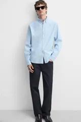 Camisa celeste de corte regular fit, confeccionada en popelín de algodón. Tiene cuello abotonado, manga larga con puños abotonados y cierre frontal con botones.