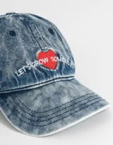 Gorra de denim celeste con efecto gastado, con bordado de corazón rojo y frase "Let's Grow Some" en blanco.