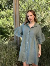 Vestido camisero azul de lino italiano, con cuello camisero, botones frontales, mangas 3/4 con doble volado y bolsillos laterales.