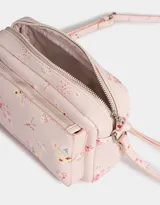 Bandolera pequeña de cuerina color rosa pálido con estampado floral multicolor. Tiene bolsillo frontal con cierre, correa regulable, cierre superior y tag metálico con logo.
