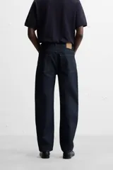 Jeans de corte slim fit confeccionados en denim de algodón sin lavados, color azul oscuro. Cierre frontal con botones y cinco bolsillos.