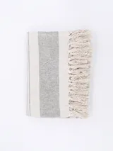 Pie de cama rectangular de algodón tejido a rayas verticales en tonos crudo y gris, con flecos en los extremos.