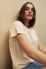 Remera de manga corta color gris claro, confeccionada en algodón con textura liviana y suave al tacto. Presenta costuras decorativas en los laterales y mangas con pequeño doblez.