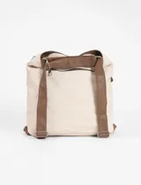 Cartera convertible en mochila color natural, con correa de hombro marrón y detalles de cierres metálicos.