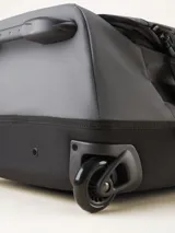 Valija gris con ruedas, manija extensible y correas de ajuste externas.