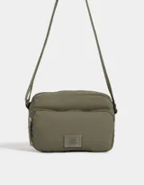 Bandolera gris claro de tela deportiva con bolsillo frontal, correa larga regulable, acceso con cierre superior y tag de goma.