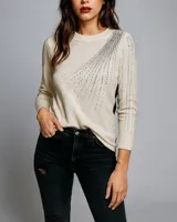 Sweater color crema de lanilla con cuello redondo y mangas largas. Presenta apliques de strass plateados en forma de rayos en el frente y en las mangas.