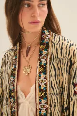 Kimono de manga ancha, estilo japonés, con estampado que imita piel de cebra en tonos beige y negro. El borde está decorado con apliques de mostacillas y bordados florales en tonos rojizos, verdes y dorados.