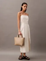 Mini cartera tote Calvin Klein color beige, confeccionada en poliuretano, con doble asa de mano y correa de hombro ajustable extraíble. Incluye cierre con botón a presión y bolsillo interior para tarjeta.