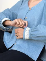 Camisa celeste de jean con cuello en V, mangas largas abullonadas con puños de encaje y cierre frontal con botones.