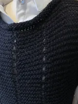 Chaleco negro tejido a mano en dos agujas con hilado 100% baby alpaca, ligeramente oversize, de hombros anchos y cuello tipo bote, con puntos calados en frente y espalda y tajos a los lados en el bajo.