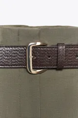 Pantalón de vestir color verde oliva, de tiro alto y pernera ancha, con pliegues delanteros, elástico en la espalda y cinturón marrón de cuero.