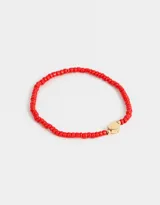Pulsera elástica de mostacillas rojas con dije de corazón dorado.