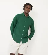 Camisa verde de lino con corte clásico, cuello camisero, manga larga y cierre frontal con botones blancos.