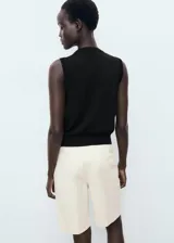 Chaleco negro de punto fino, sin mangas, con tirantes anchos, diseño recto, cuello de pico y cierre delantero con botones.