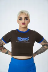Remera corta marrón con cuello y mangas con ribete azul, estampado frontal con la palabra "Hermod" en celeste y la frase "Eternal soul, divine flow" en blanco.