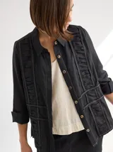 Camisa negra de lino con corte femenino, cuello clásico, cierre frontal con botones y mangas 3/4 con puños enrollados. Presenta detalles de frunces verticales en el frente y bolsillos de parche a la altura de la cadera.