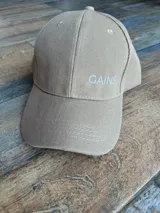 Gorro color beige con visera y bordado frontal con la palabra "GAINS" en color blanco.